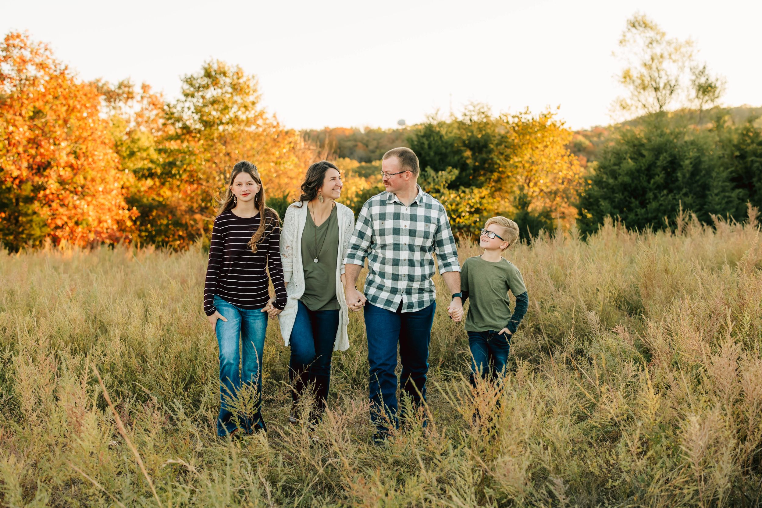 A family of four stands together in a fall field during golden hour.