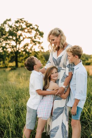 A family shares a tender moment together in a sunlit field with trees in the background.