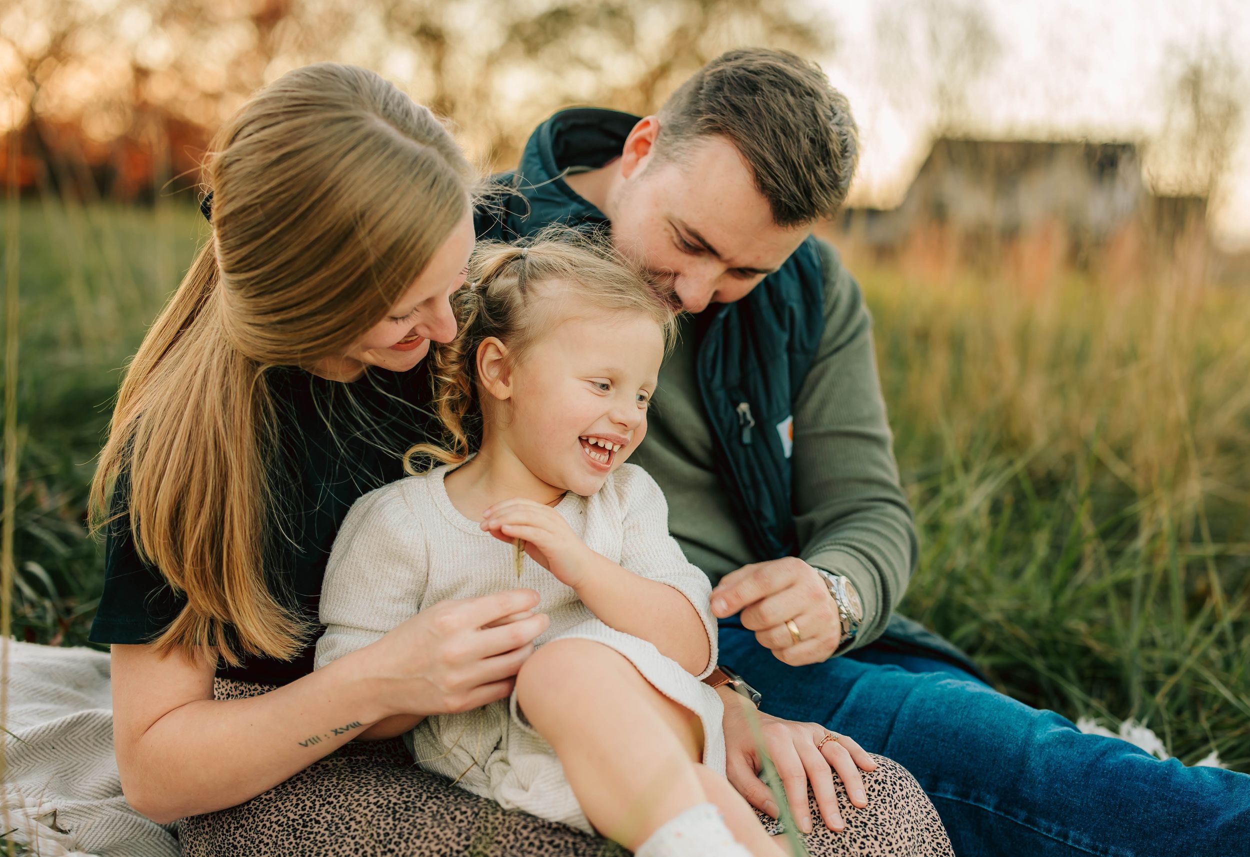 A family shares an intimate moment together while sitting in tall grass at sunset.