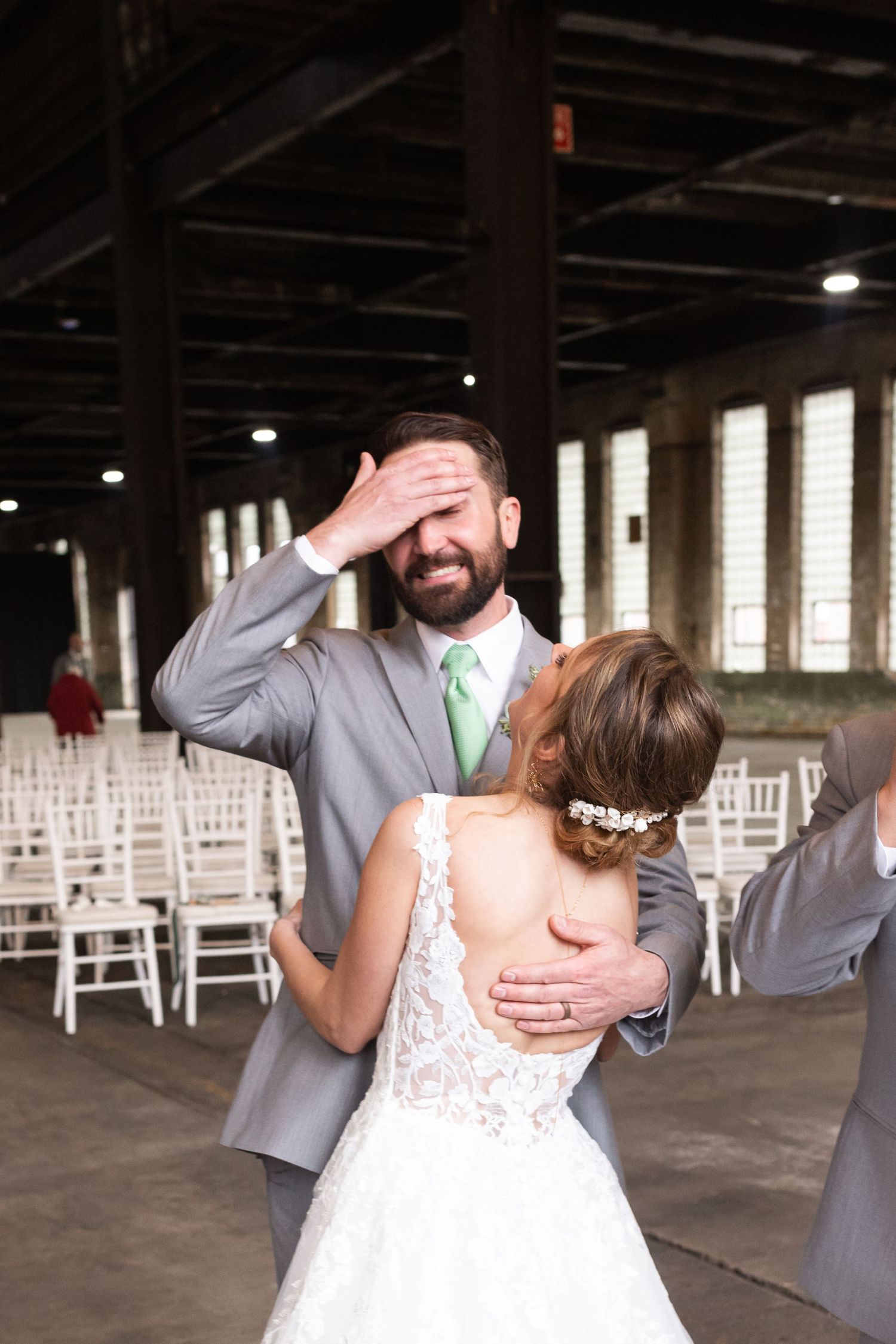 Wedding celebration in industrial venue with white chairs and exposed beam ceiling.