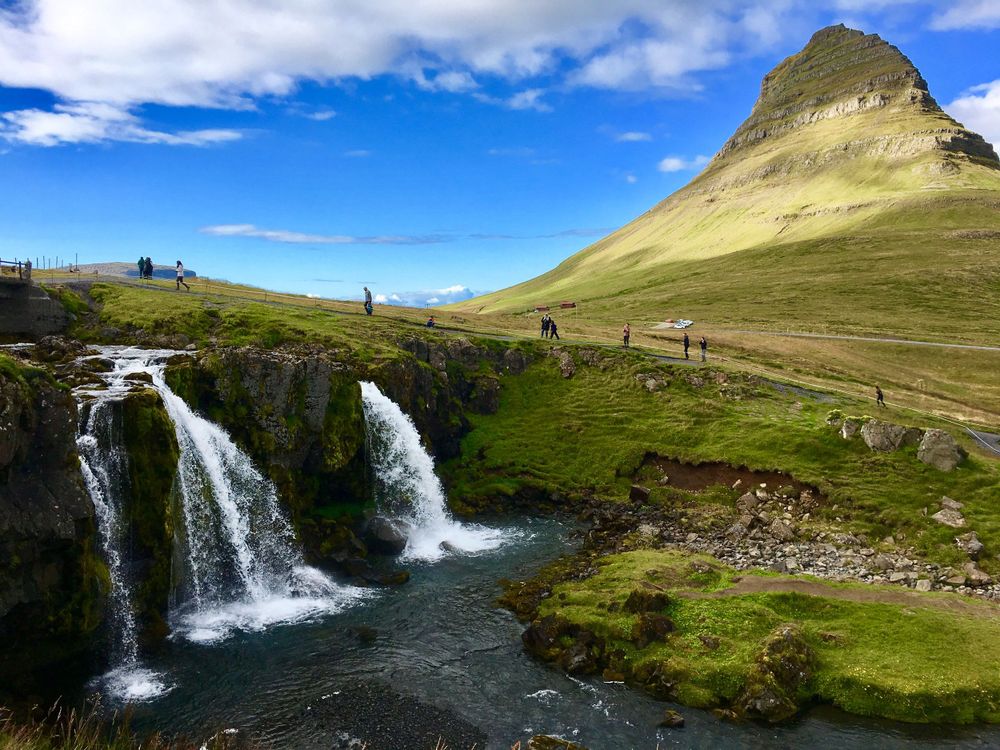Scenic waterfall cascading down green cliffs in a mountainous landscape.
