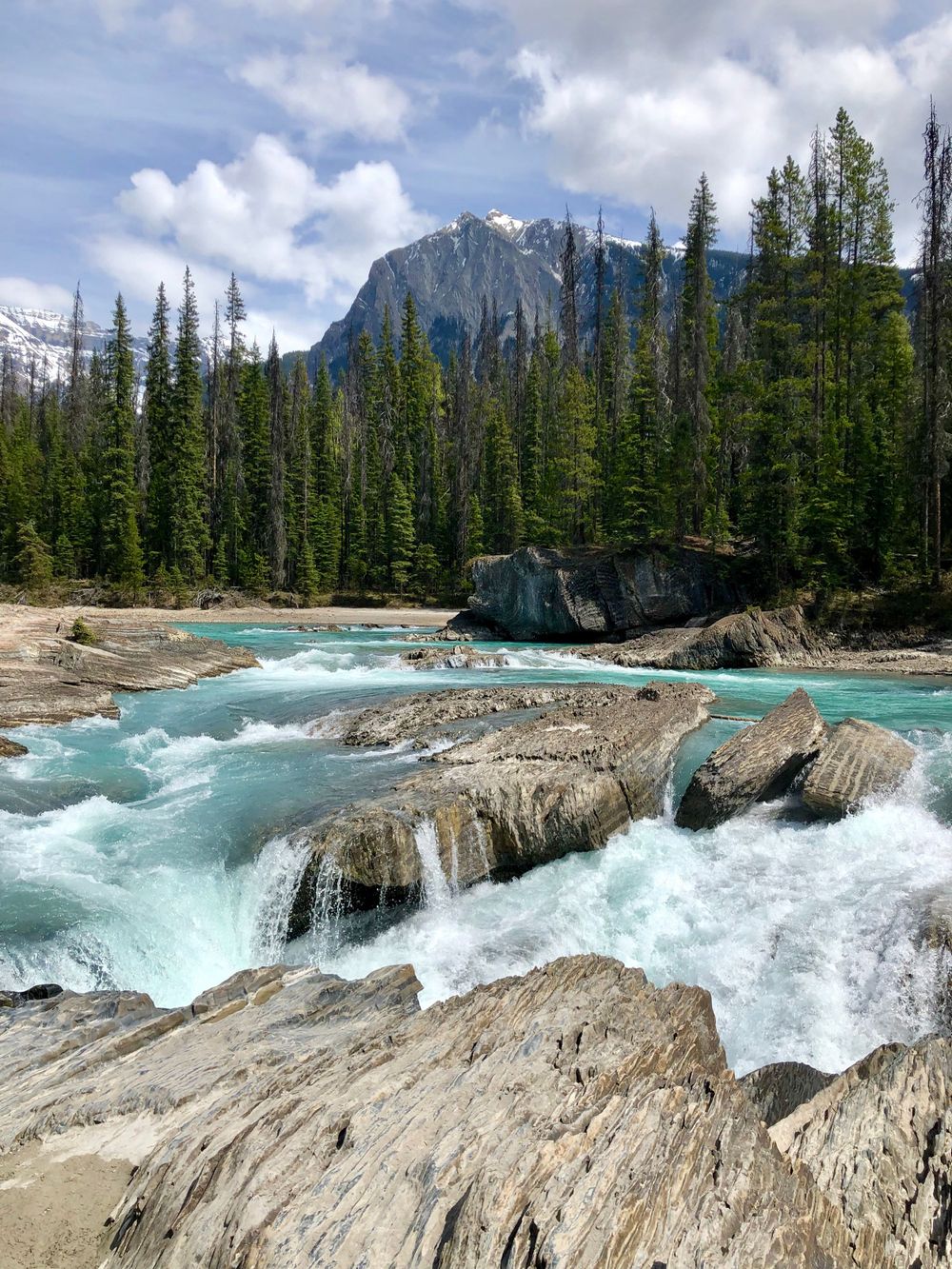 Turquoise waterfall cascading over rocky terrain in a mountainous forest setting.