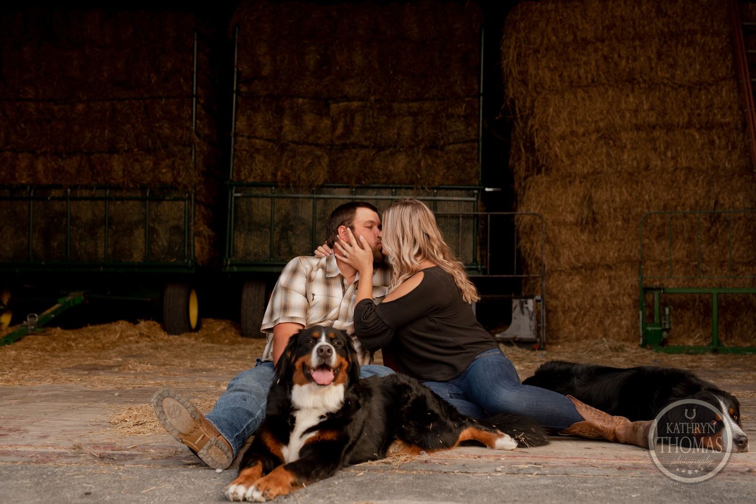 Intimate couple moment with their dogs in a cozy barn setting.