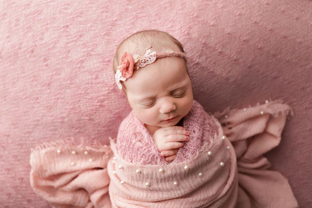 fine art newborn studio portrait of baby girl in pink with headband and pearls