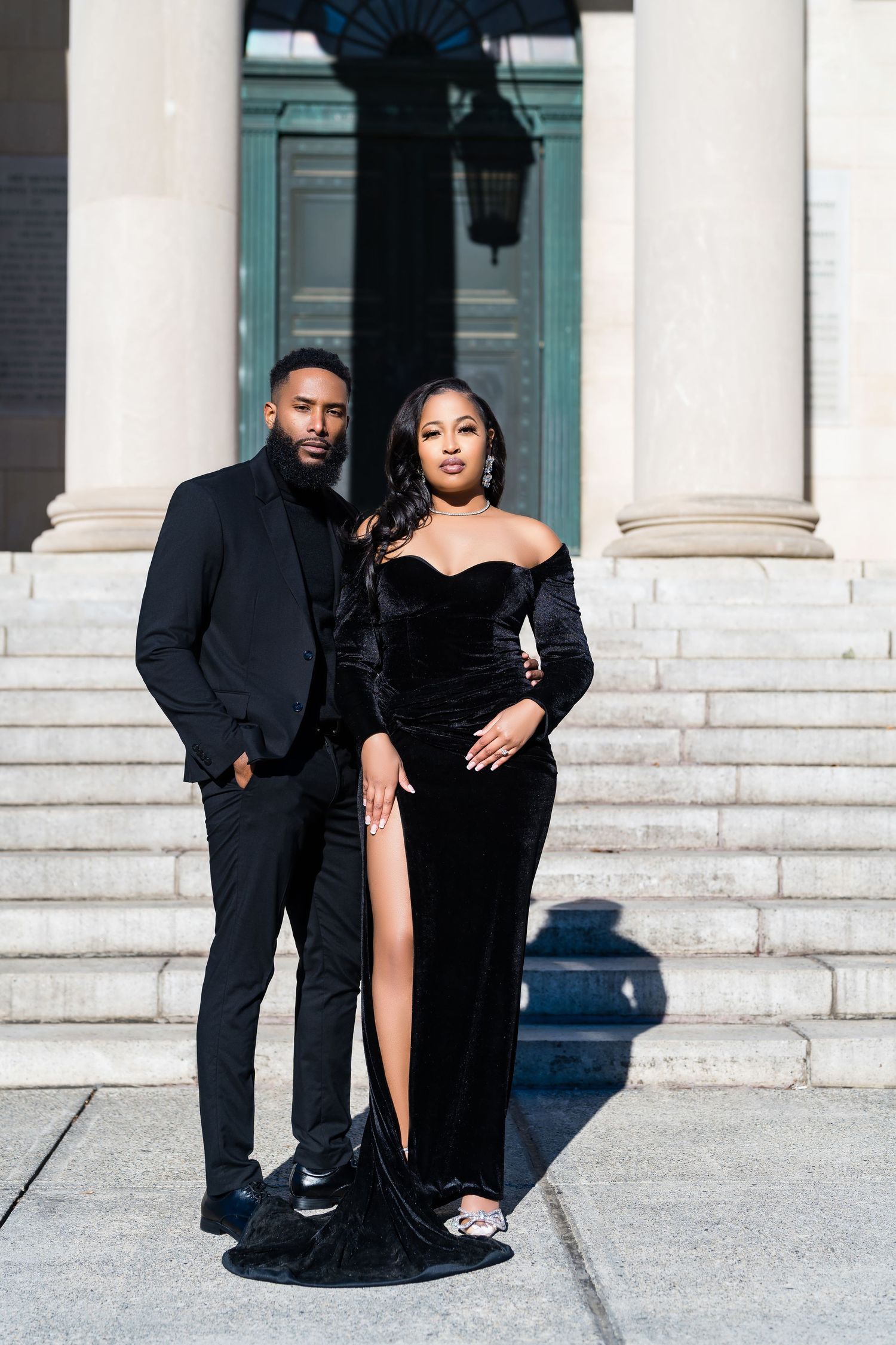 A couple in formal black attire poses on white stone steps in front of a teal door.