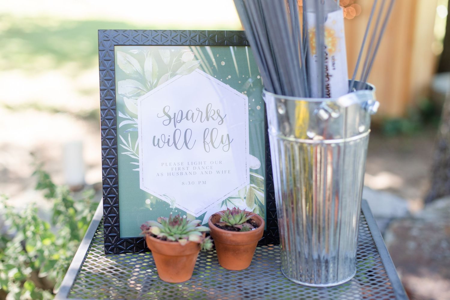 Wedding decor details featuring small potted succulents and elegant signage.