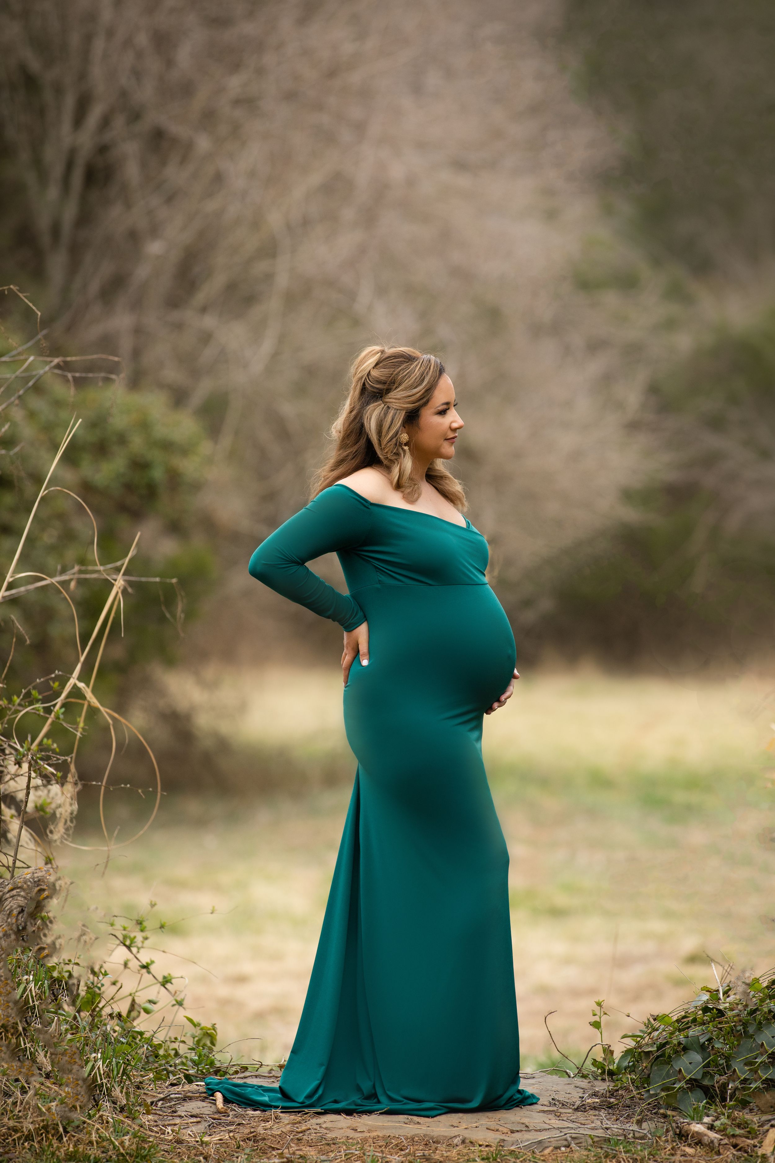 Elegant maternity portrait of an expectant mother in a teal dress outdoors.