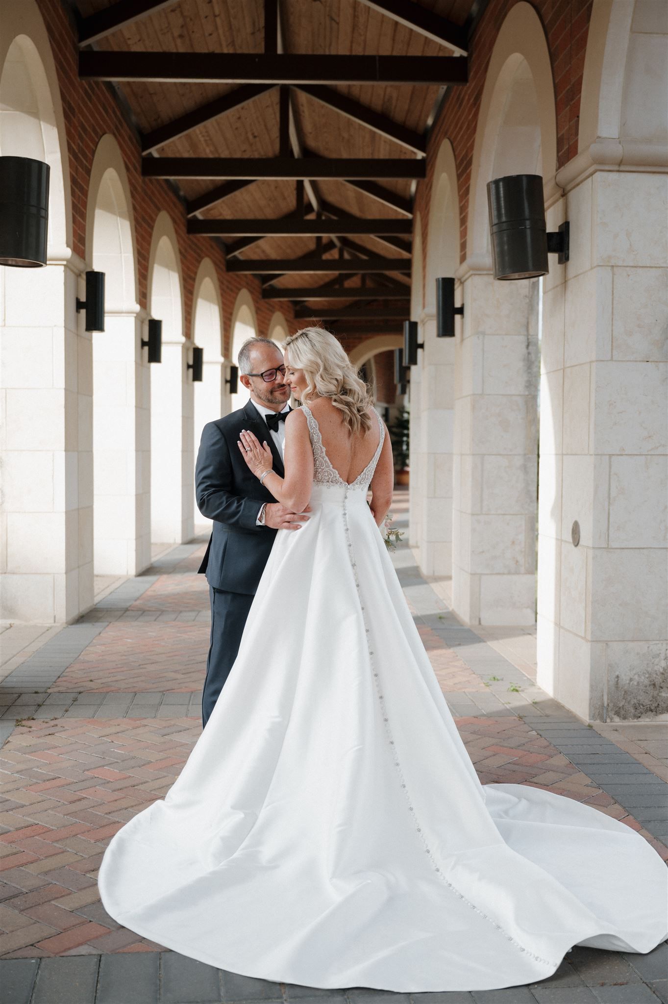 Elegant bride and groom pose in archway with dramatic wedding dress train.