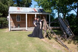 A couple poses in front of a rustic wooden cabin with a tin roof.