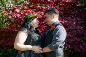 A couple embraces in front of vibrant red maple leaves during their wedding.