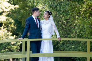 Newlyweds pose together on a green garden bridge surrounded by lush foliage.