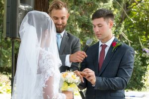 A wedding ceremony moment as groomsmen assist with adjusting the bride's veil outdoors.