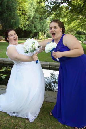 Wedding party members strike playful poses with bouquets in a garden setting.