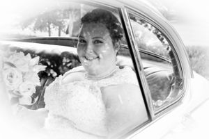Monochrome portrait of someone in a wedding dress smiling through a car window.
