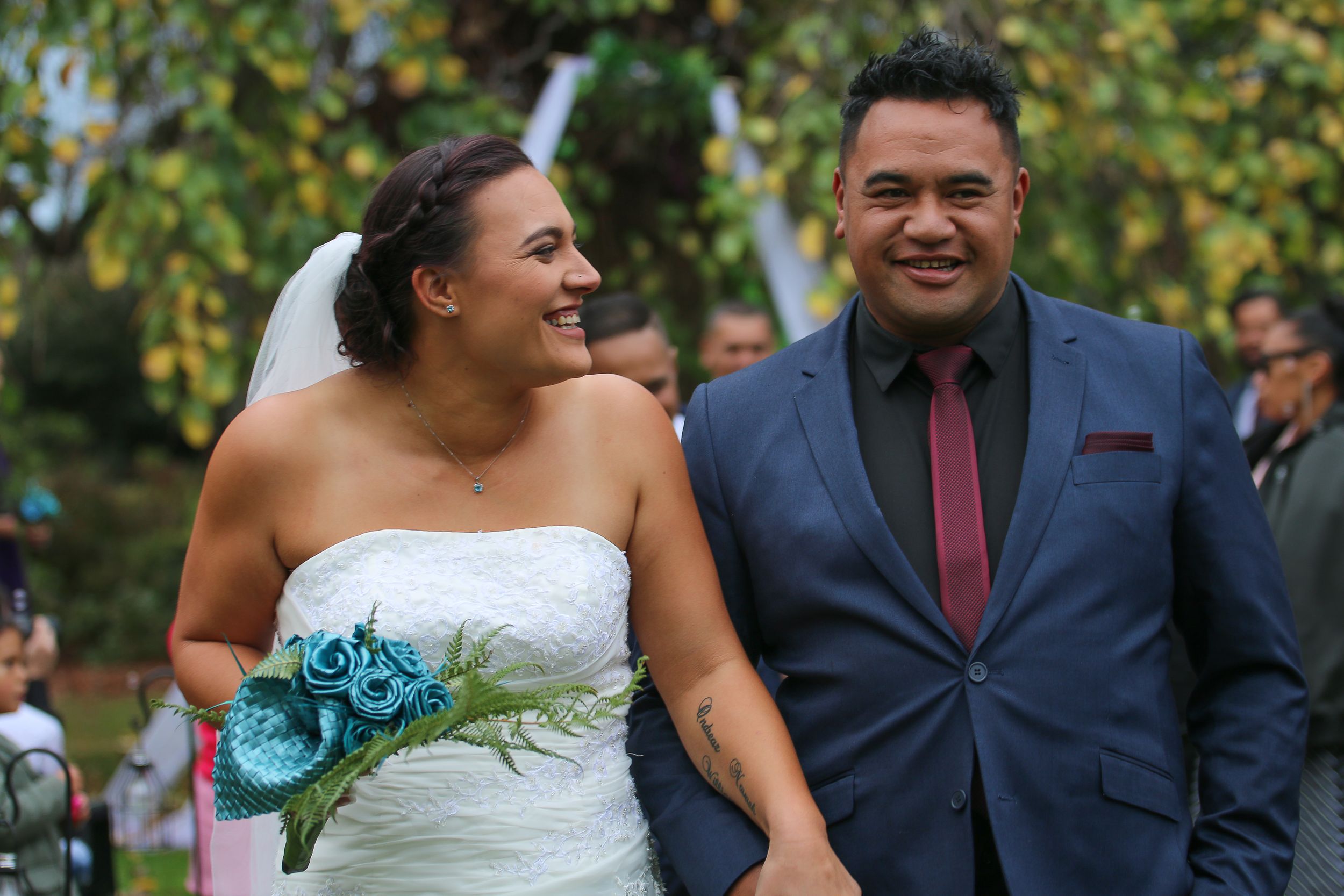 Happy newlyweds share a joyful moment with bride holding blue flowers in garden setting.