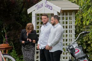 Three people standing near a white garden arbor during an outdoor ceremony.