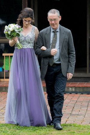 An elegant duo in formal attire walking along a brick pathway.