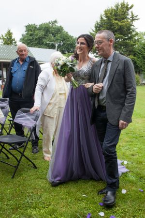 A wedding party in formal attire standing on grass near folding chairs.