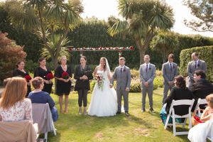 An outdoor wedding ceremony in a garden setting with palm trees and white chairs for guests.