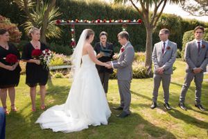 Wedding ceremony taking place under a decorated arch with palm trees and garden landscaping.