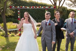 Emotional wedding celebration moment in a scenic garden with palm trees and decorative arch.