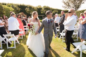 Newlyweds walk down the aisle while guests applaud in an outdoor garden setting.
