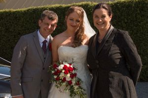 Wedding portrait in front of hedge with red and white bouquet details.