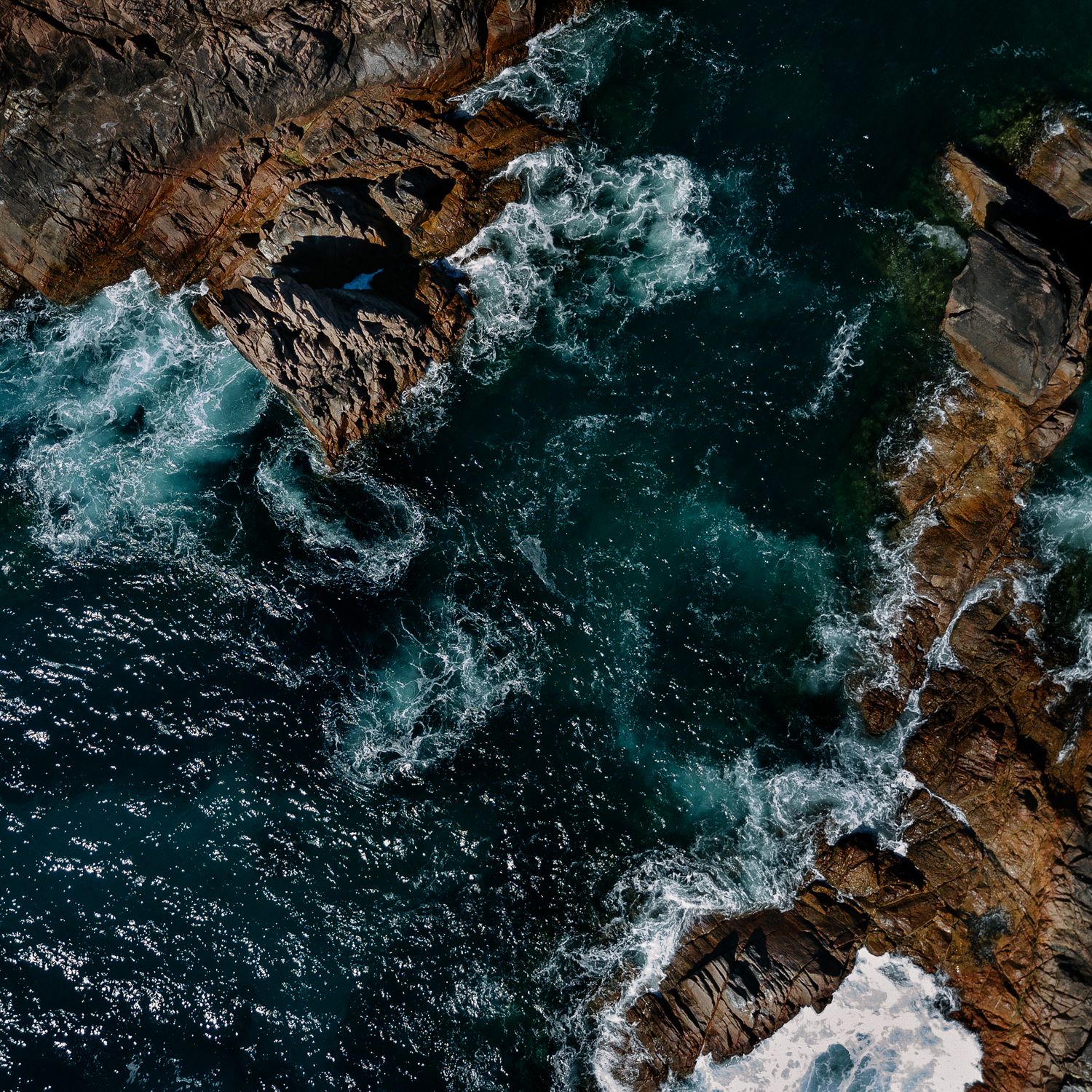 Aerial view of rugged coastline where turquoise ocean waves crash against rocky cliffs.