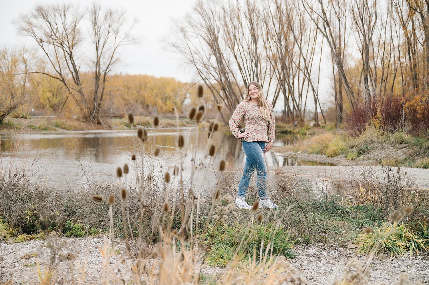 A casual outdoor portrait by a river with dried cattails and bare trees in autumn.
