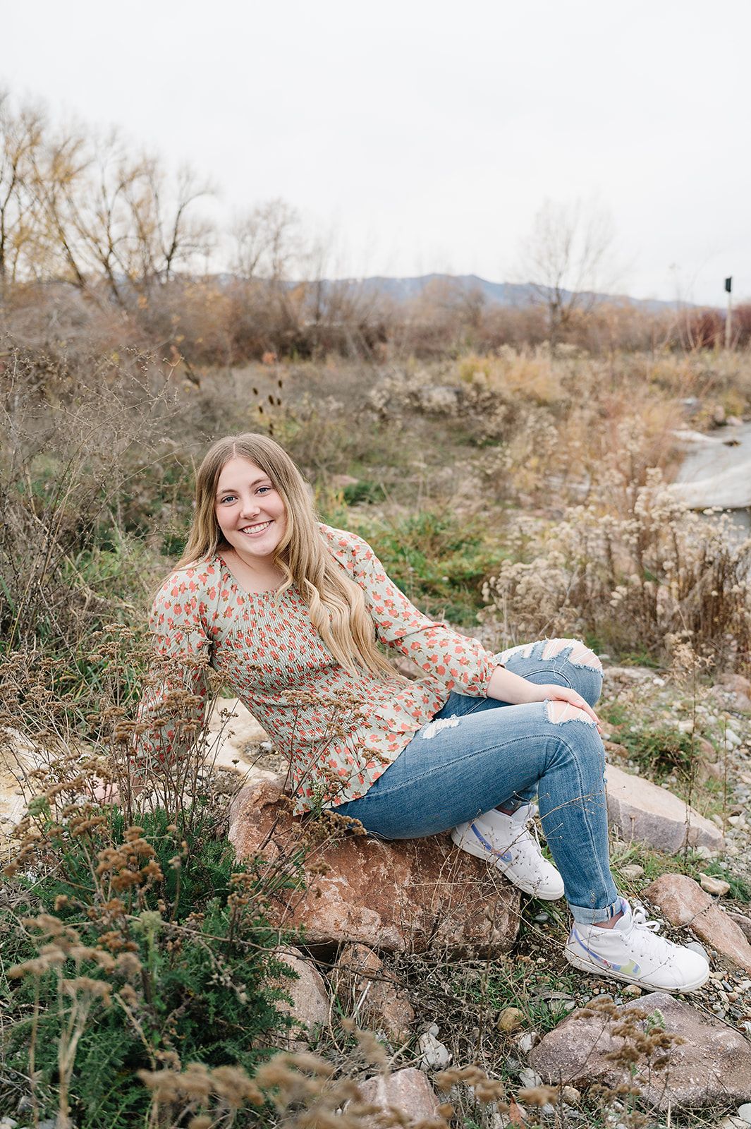 A relaxed outdoor portrait on a rocky outcrop beside a winding stream.