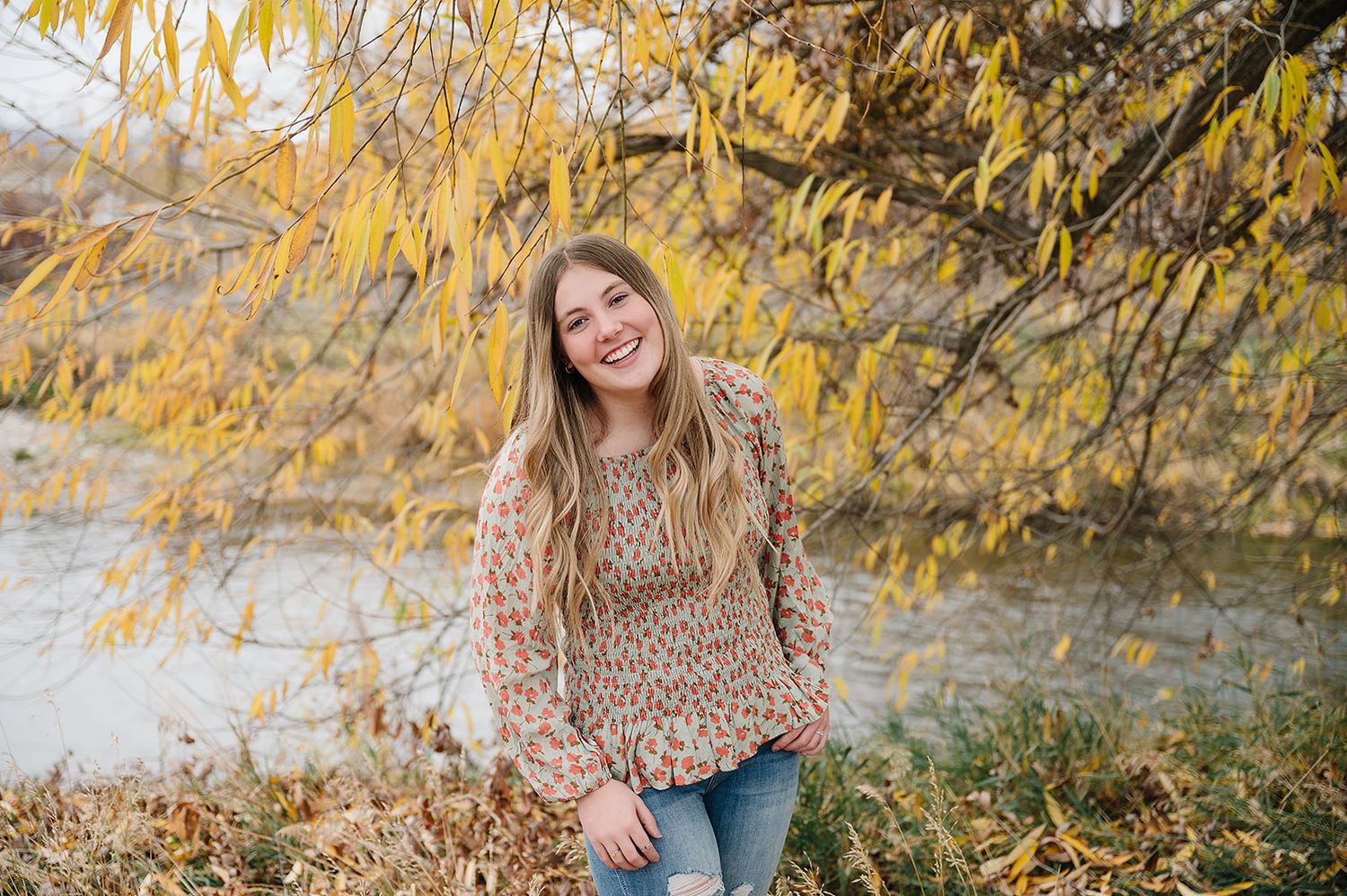 A joyful autumn portrait under yellow willow branches near a flowing stream.