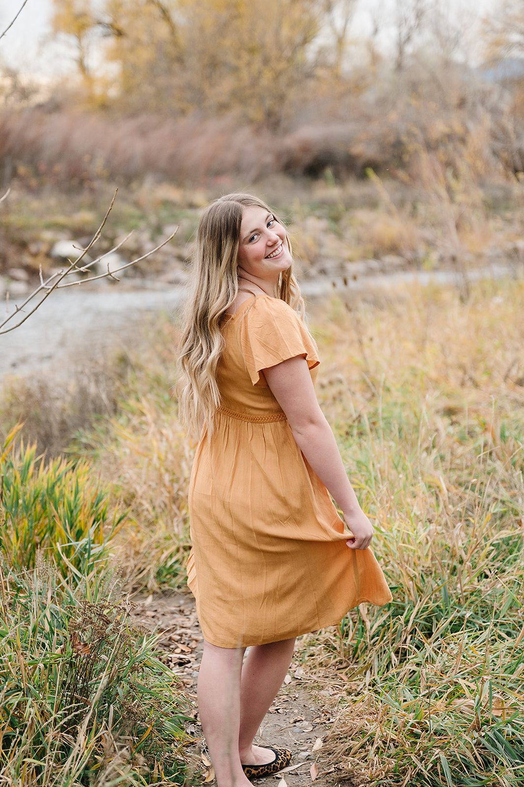 A carefree outdoor portrait in a mustard dress among autumn grasses by the riverbank.