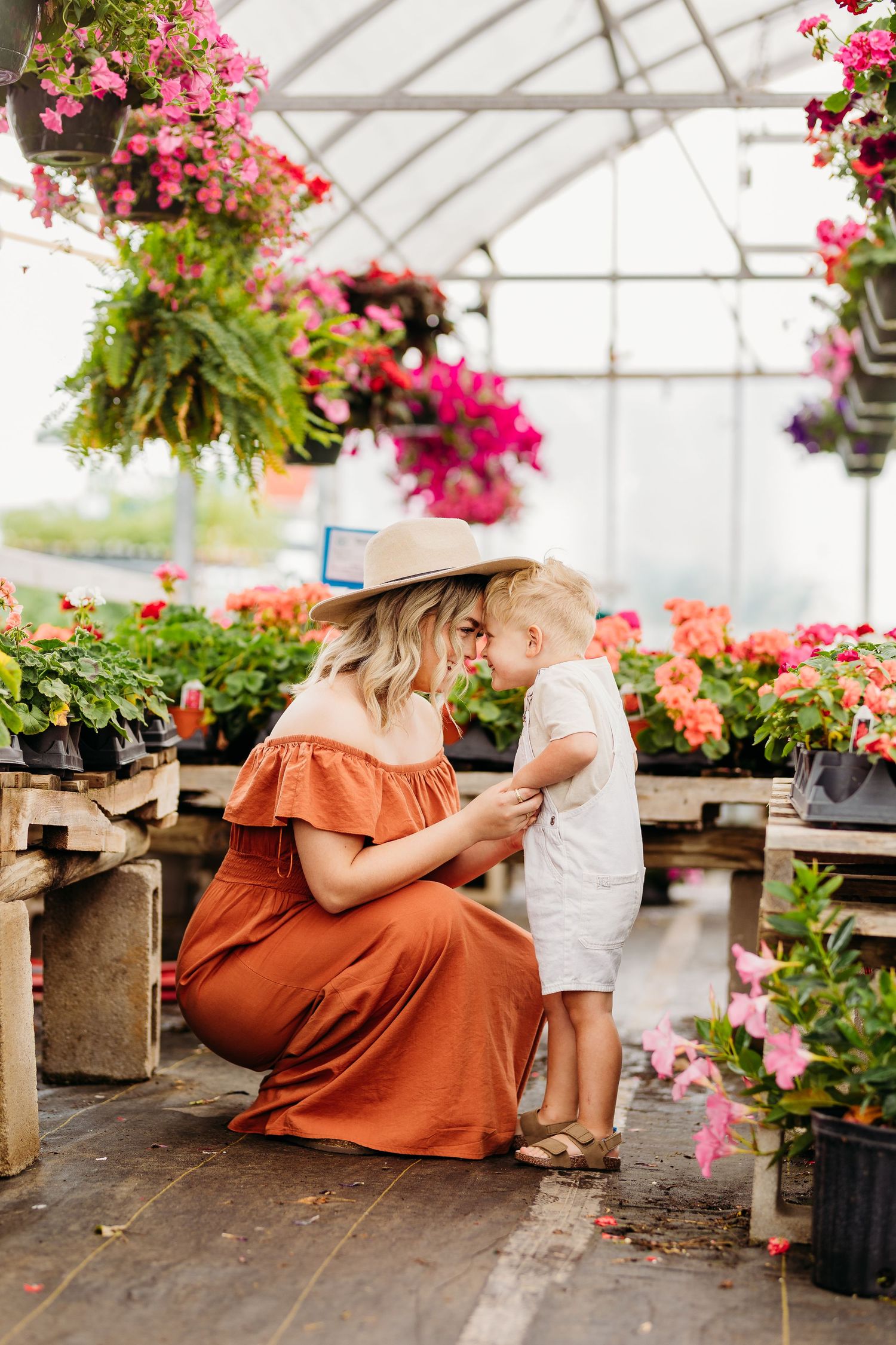 Tender moment in greenhouse surrounded by hanging flowers and potted plants.