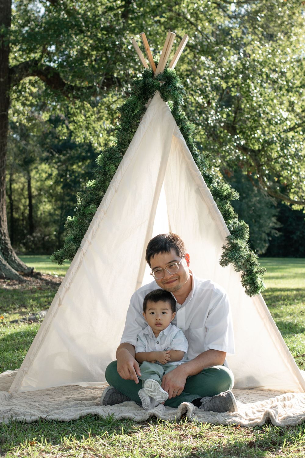 A parent and child sit together in front of a decorated white teepee tent.