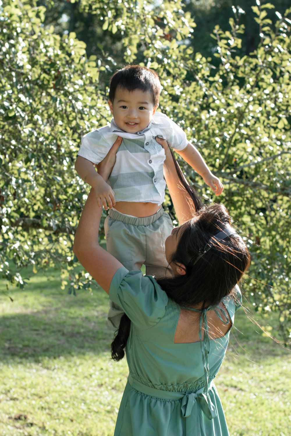 A joyful moment in a sun-dappled garden as parent lifts small child high in the air wearing matching mint green outfits.
