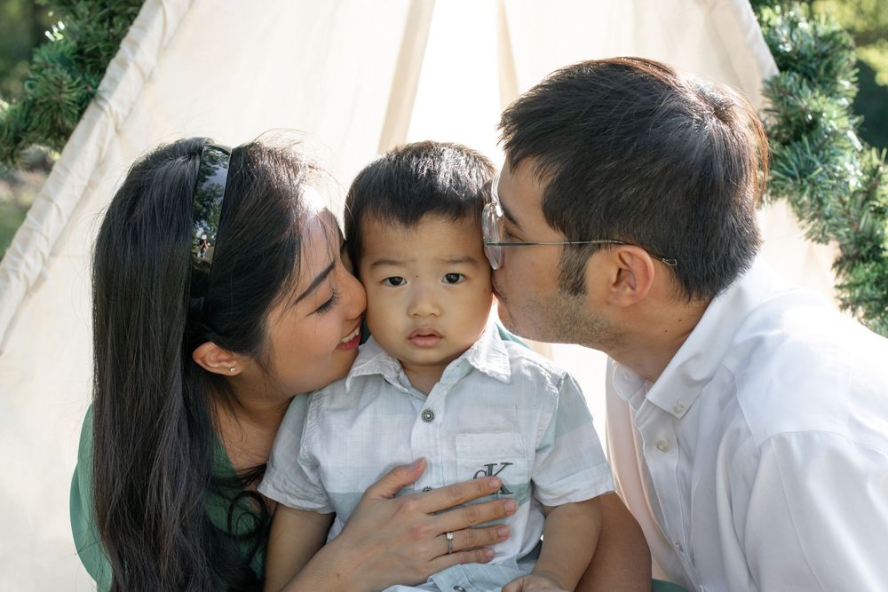 Parents share loving kisses with their young child outdoors.
