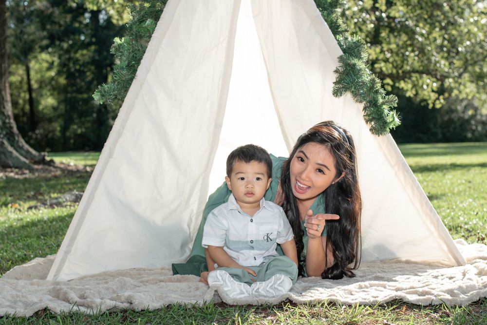 A mother and child pose together in front of a white teepee tent outdoors.