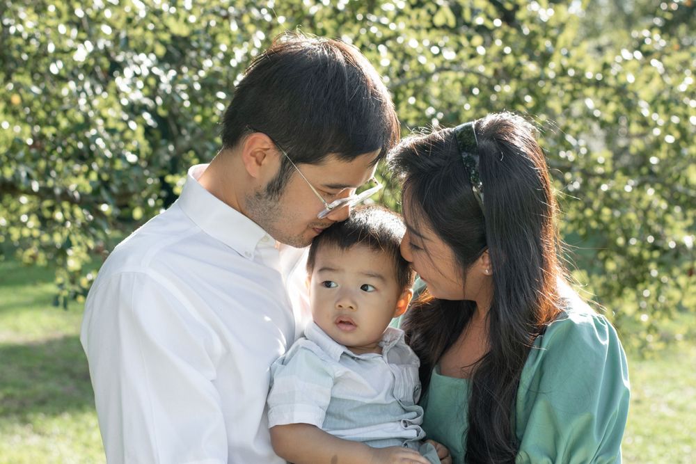 A family embraces while holding their young child in an outdoor setting.