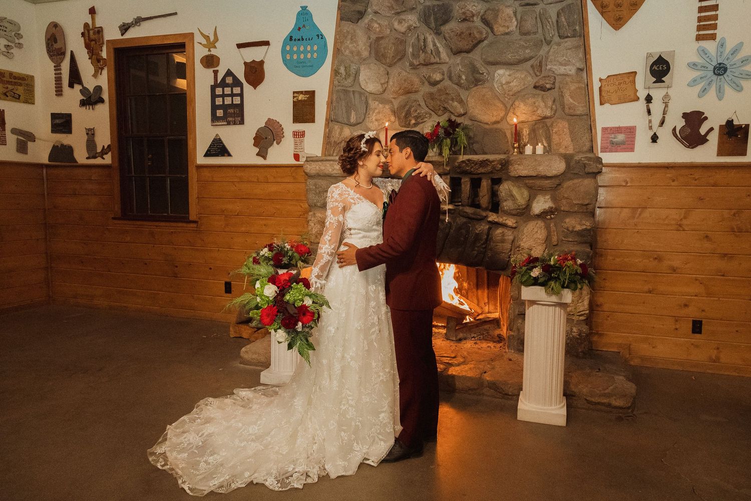 Couple shares romantic moment by stone fireplace with rustic wooden walls and colorful floral arrangements.