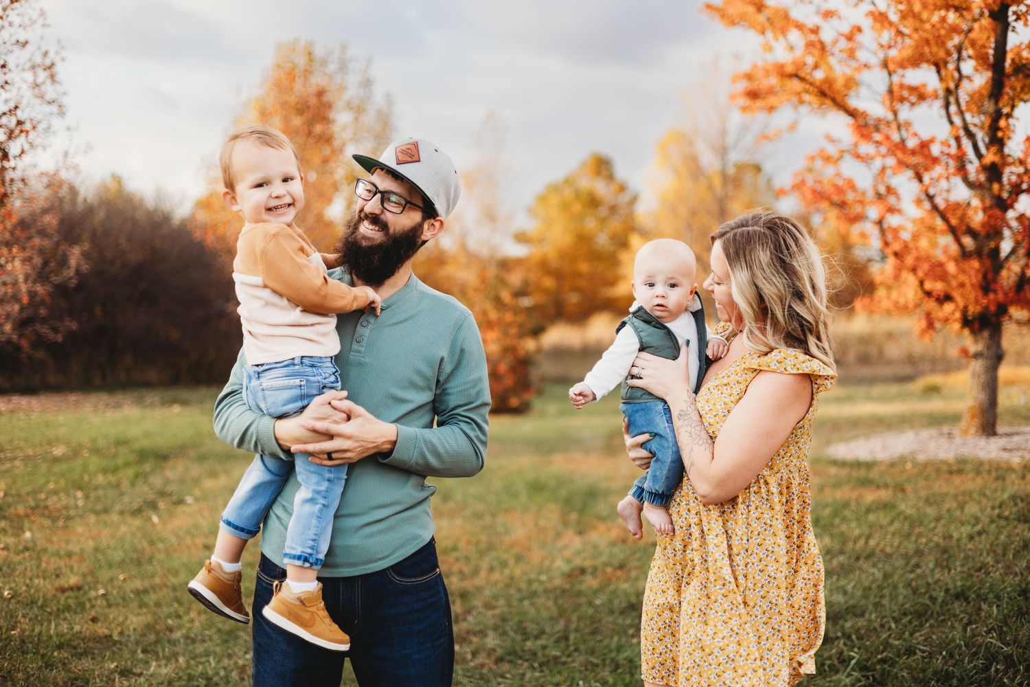 Family autumn portrait with toddlers and parents in a park with colorful fall foliage.