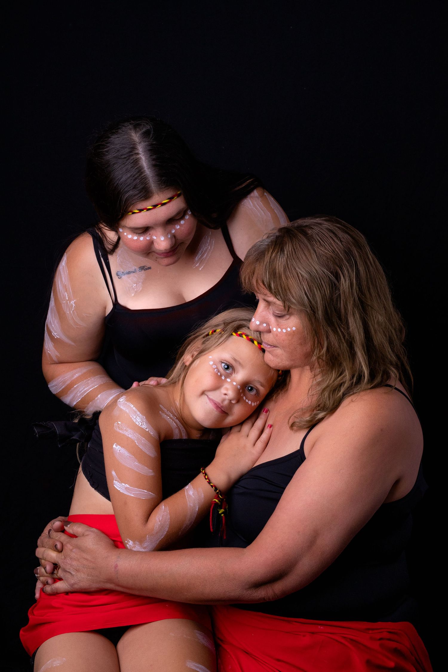 Grandmother, Mother and child wearing Aboriginal colours of yellow, black red, headbands and traditional body paint.