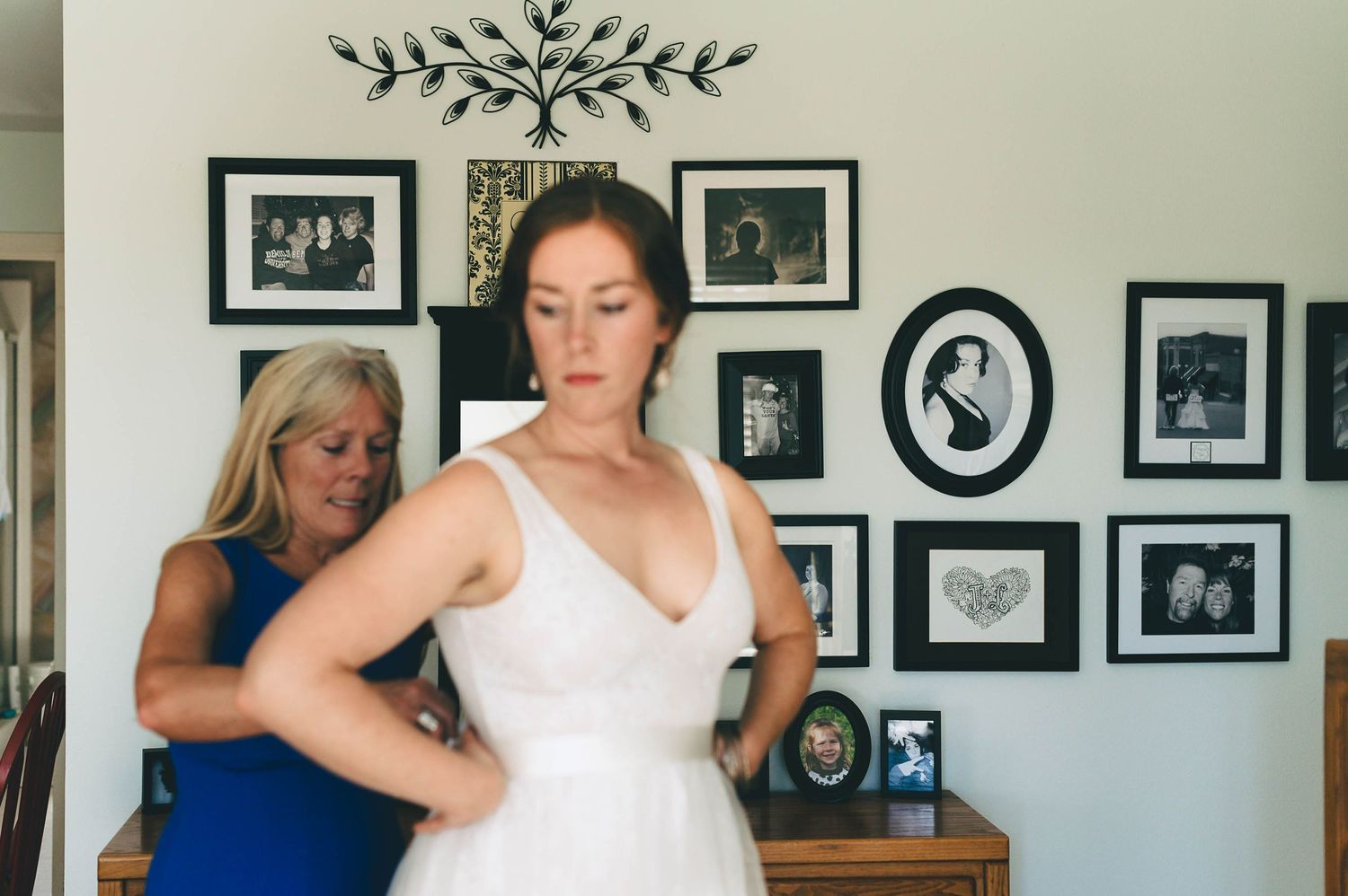 bride getting into wedding dress in front of wall with old family pictures
