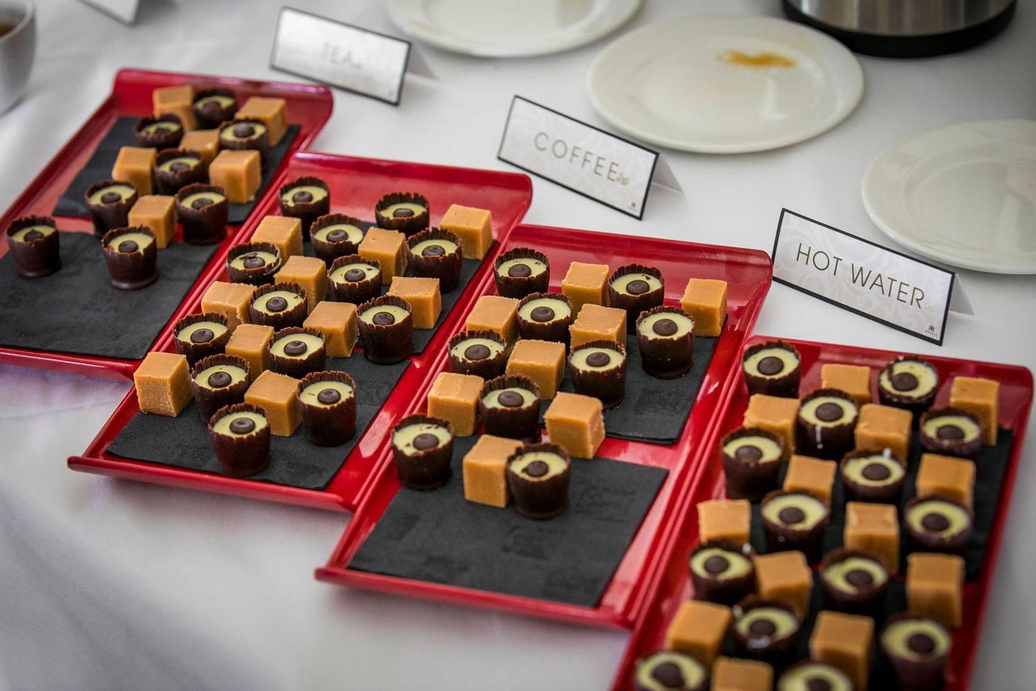 Elegant chocolate truffles arranged on red serving platters with name cards at a catered event.