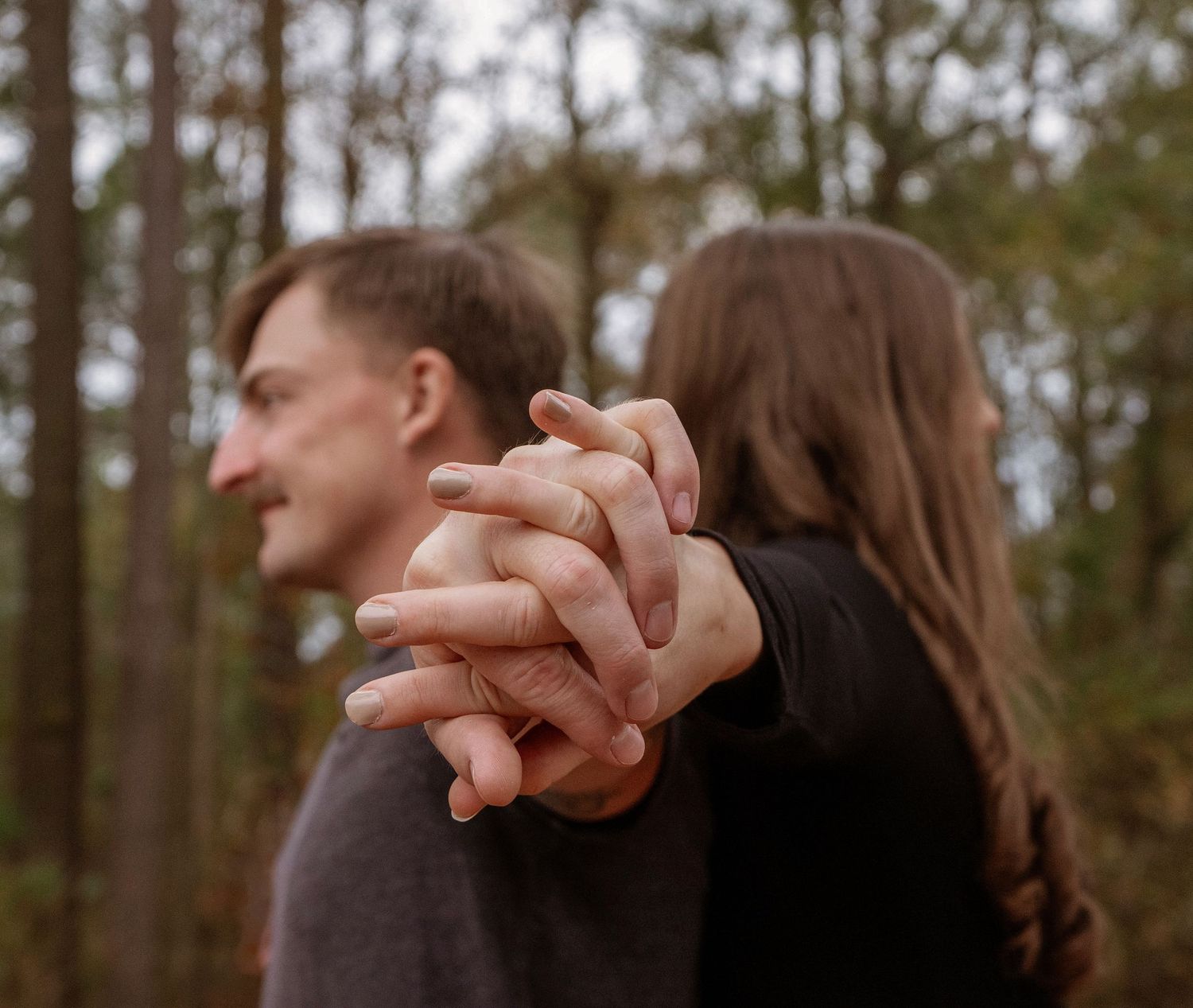 Close up of intertwined hands with couple standing in a wooded forest setting.
