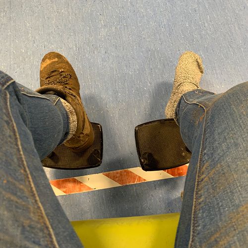 A person wearing jeans and brown shoes stands across a hazard warning stripe.