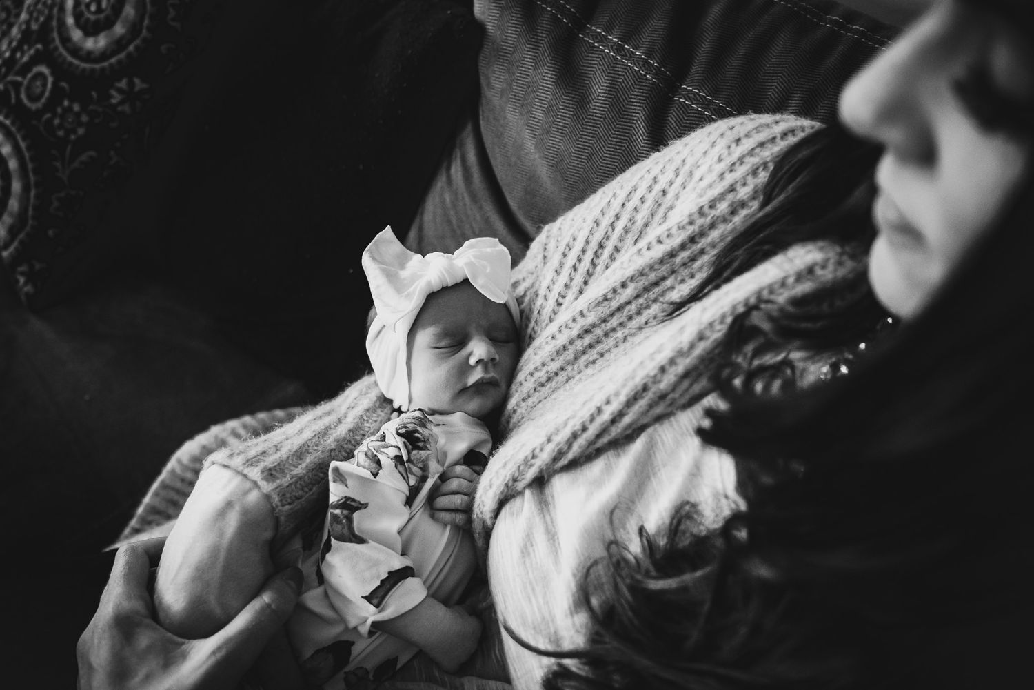 A newborn baby girl wears a giant head bow as she's held by her mama.