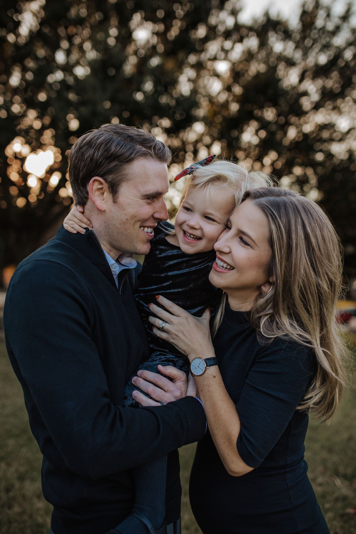 Family of three hugging and laughing at golden hour