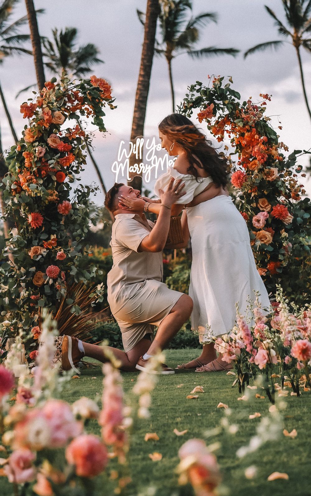 Wedding celebration moment captured under a floral arch with palm trees in the background.