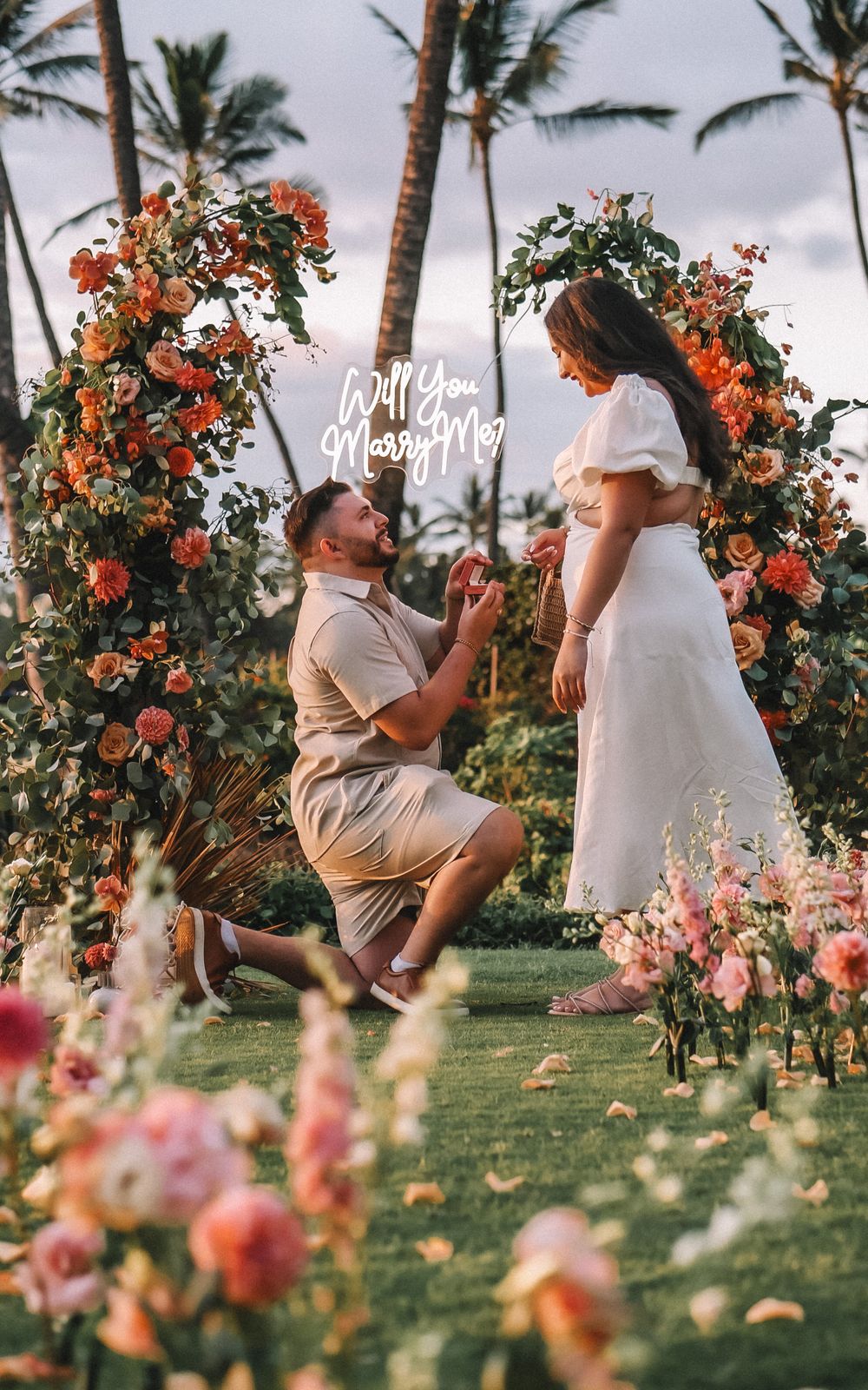 Romantic wedding ceremony setup on a tropical beach with palm trees and floral decorations.