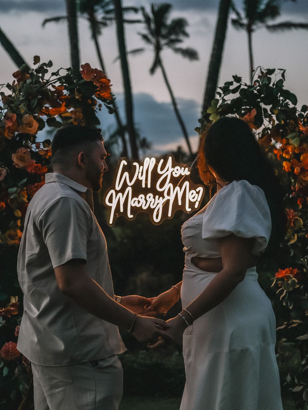 A couple shares an intimate moment at dusk with glowing text overlays and tropical foliage.